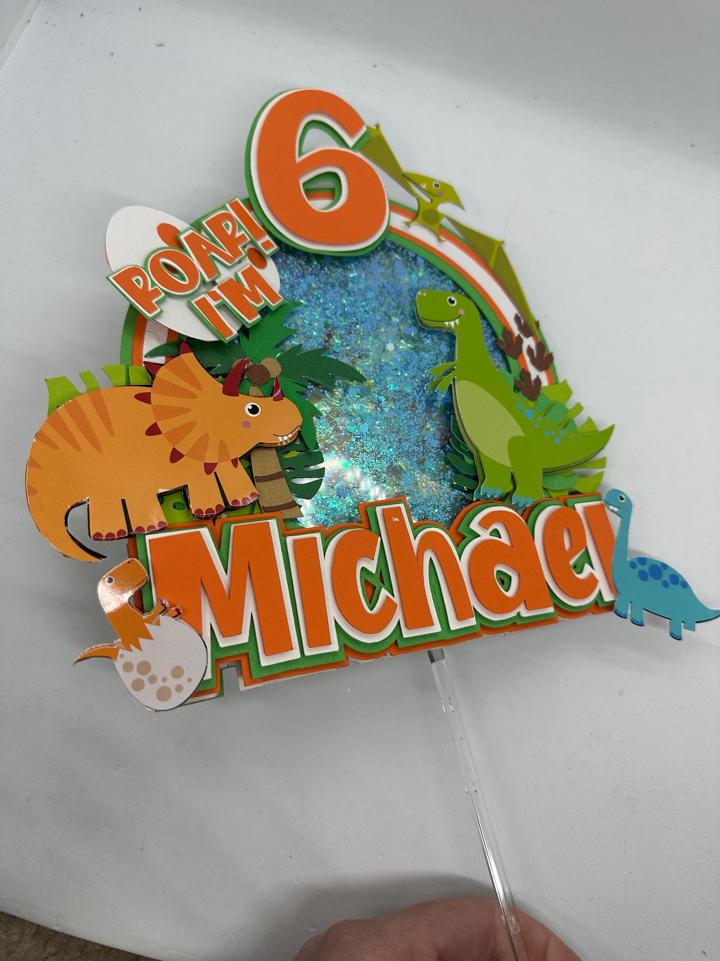 Custom dinosaur "Roar Im 6" cake topper with orange, green and white. Displaying orange and green dinosaurs