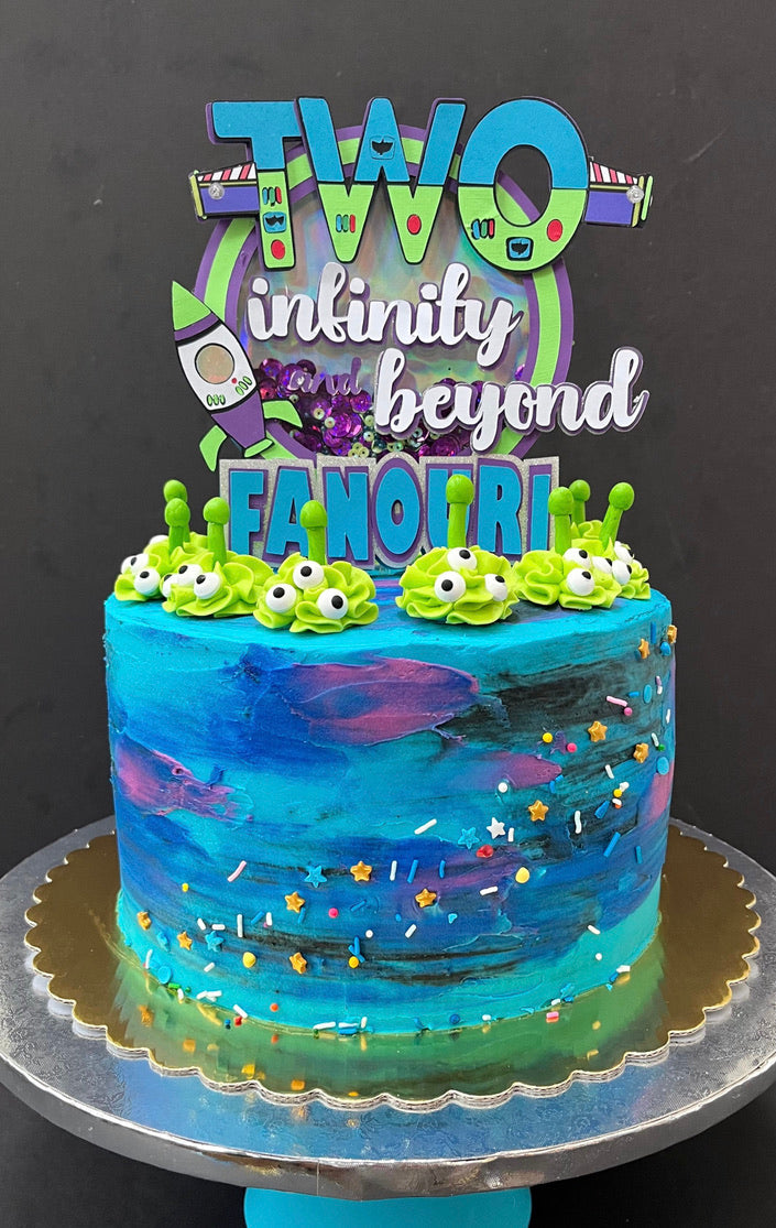 A cake with a blue and purple themed icing and a green cake topper with the text 'TWO infinity beyond' and decorative elements.