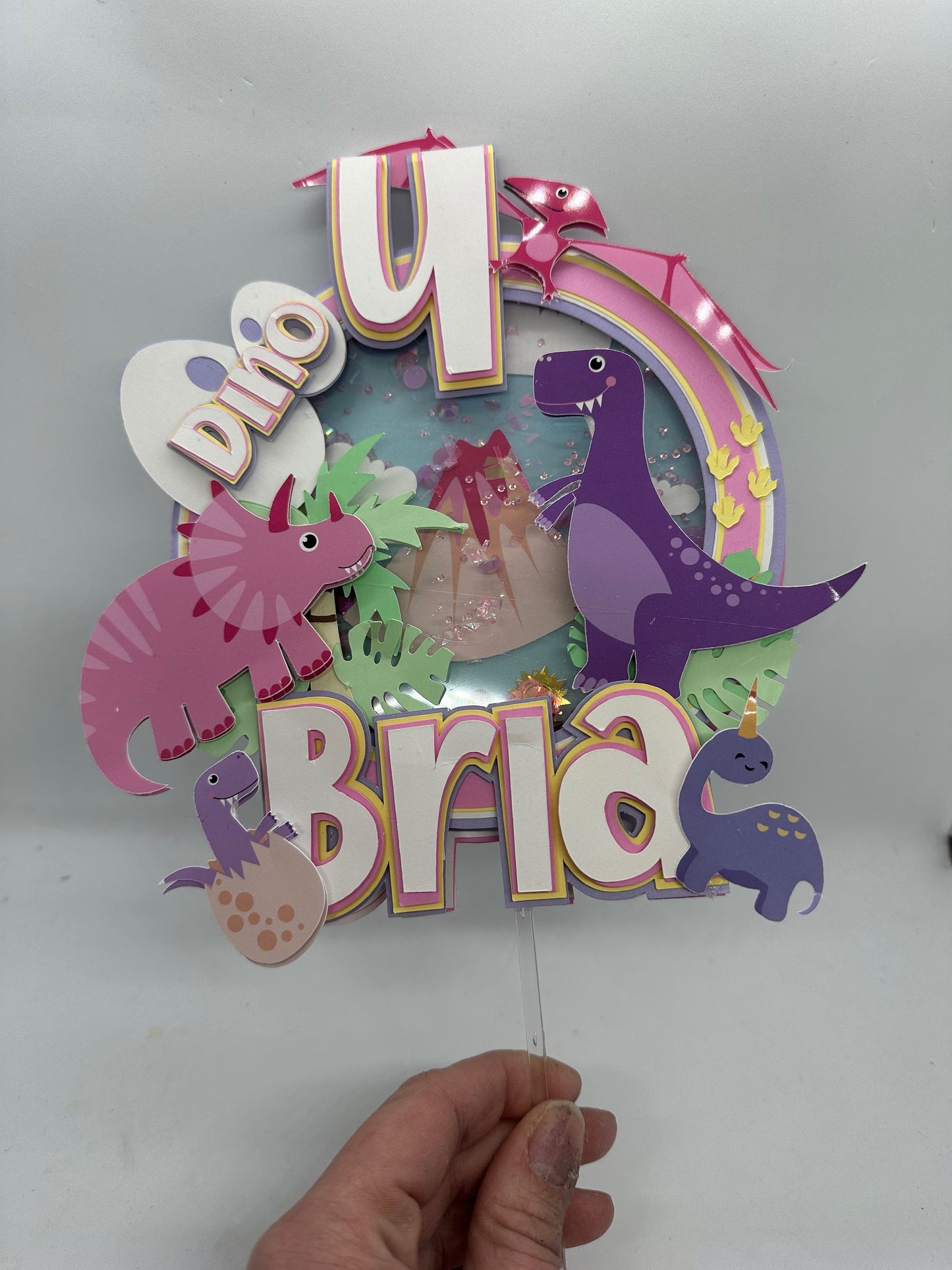 Custom dinosaur "Dino 4" cake topper with pinks, yellows and purples. Pink and purple dinosaurs
